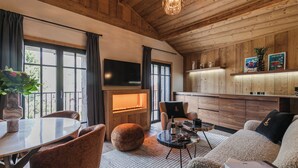 A cozy living room with a fireplace, wooden walls, a television, and a dining area with a table and chairs. - L'Écrin  (Megève)