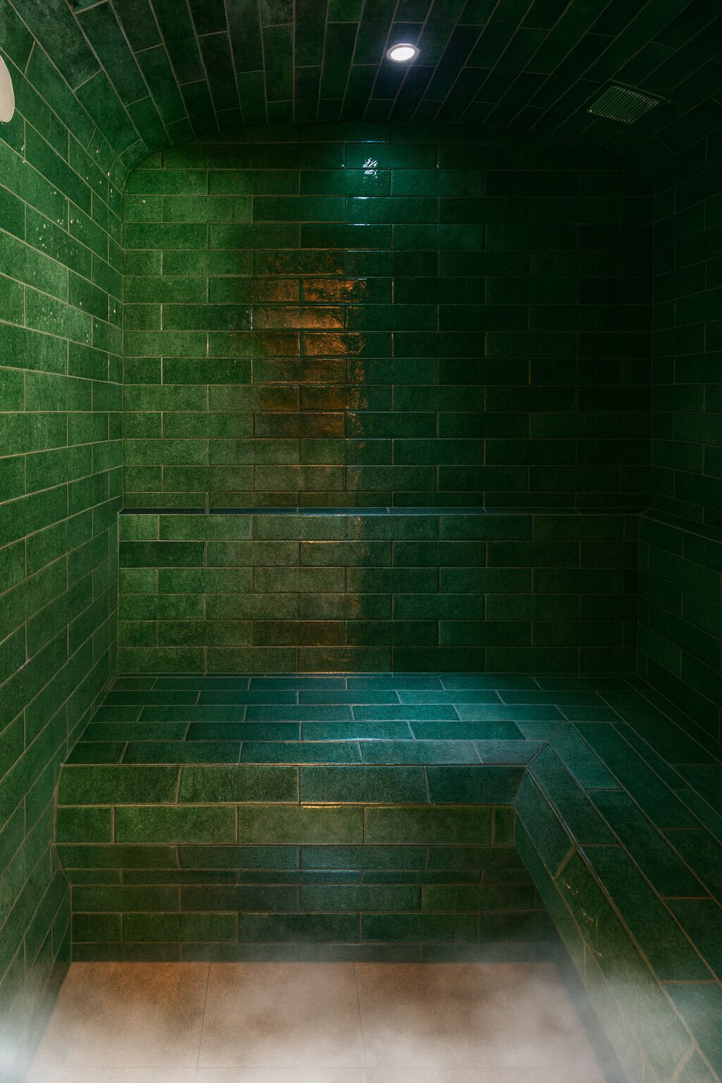 A steam room with green-tiled walls and a bench.