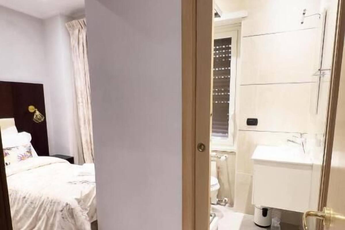 A hotel room with a bed, a bathroom with a toilet and sink, and a door leading to another room.