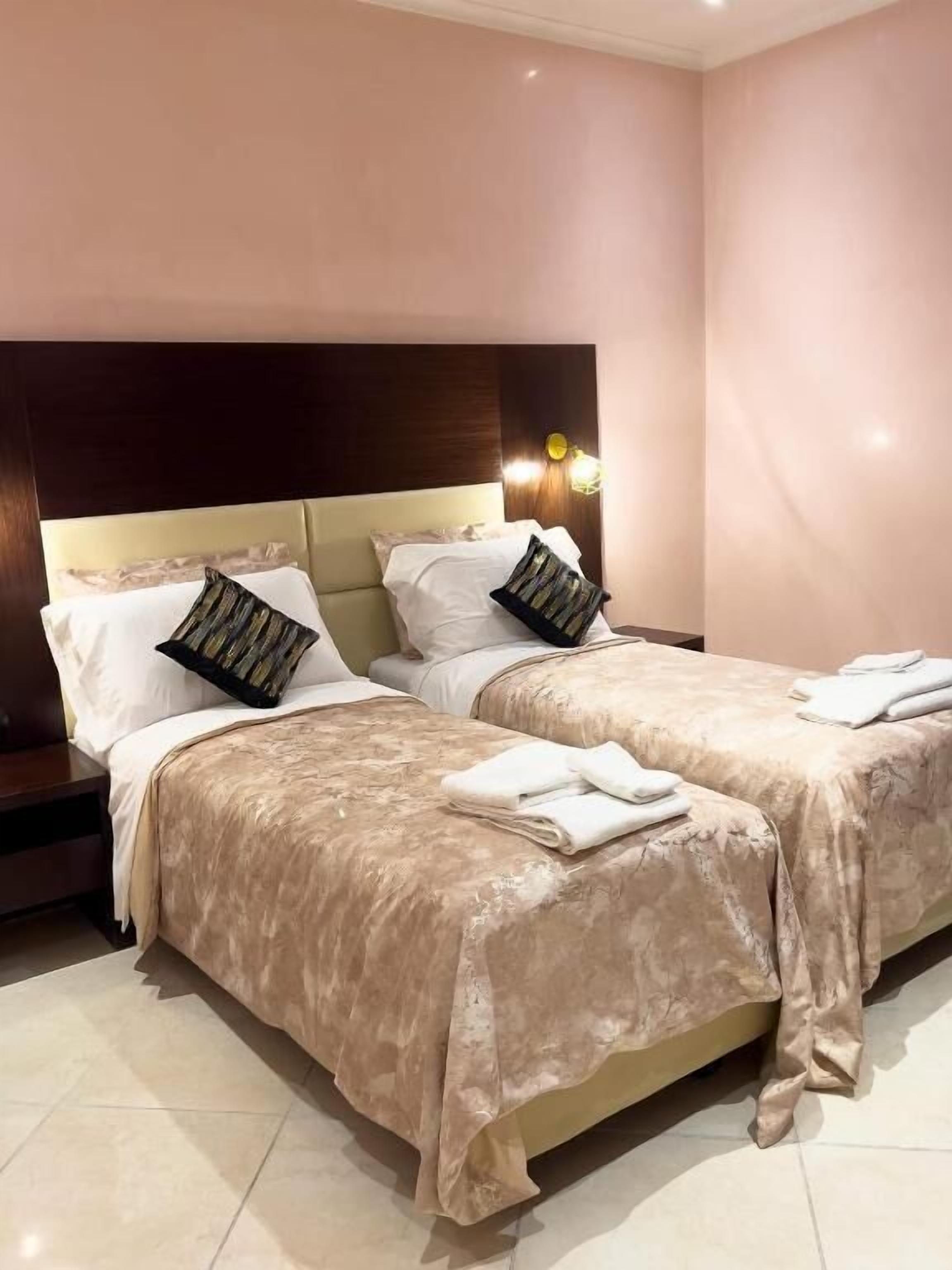 Camera d'albergo con due letti, una testiera, comodini e una lampada a parete.