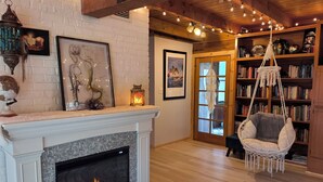 A cozy living room with a fireplace, a hanging chair, and a bookshelf.