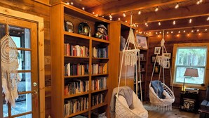 A cozy room with wooden walls, a large bookshelf, macramé hanging chairs, and a small stool.