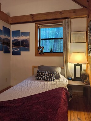 Un dormitorio con cama, una mesita de noche con lámpara, una ventana con cortinas y decoración en la pared.