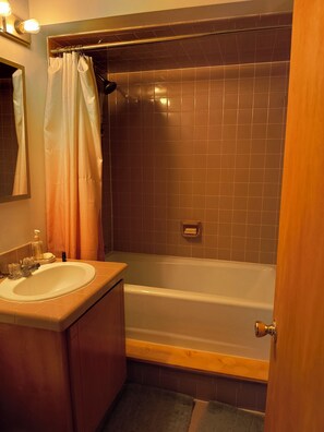 Un baño con bañera, lavamanos, espejo y toallero.