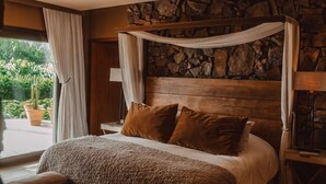 Een slaapkamer met een stenen muur, een hemelbed, een houten bankje en uitzicht op groen.