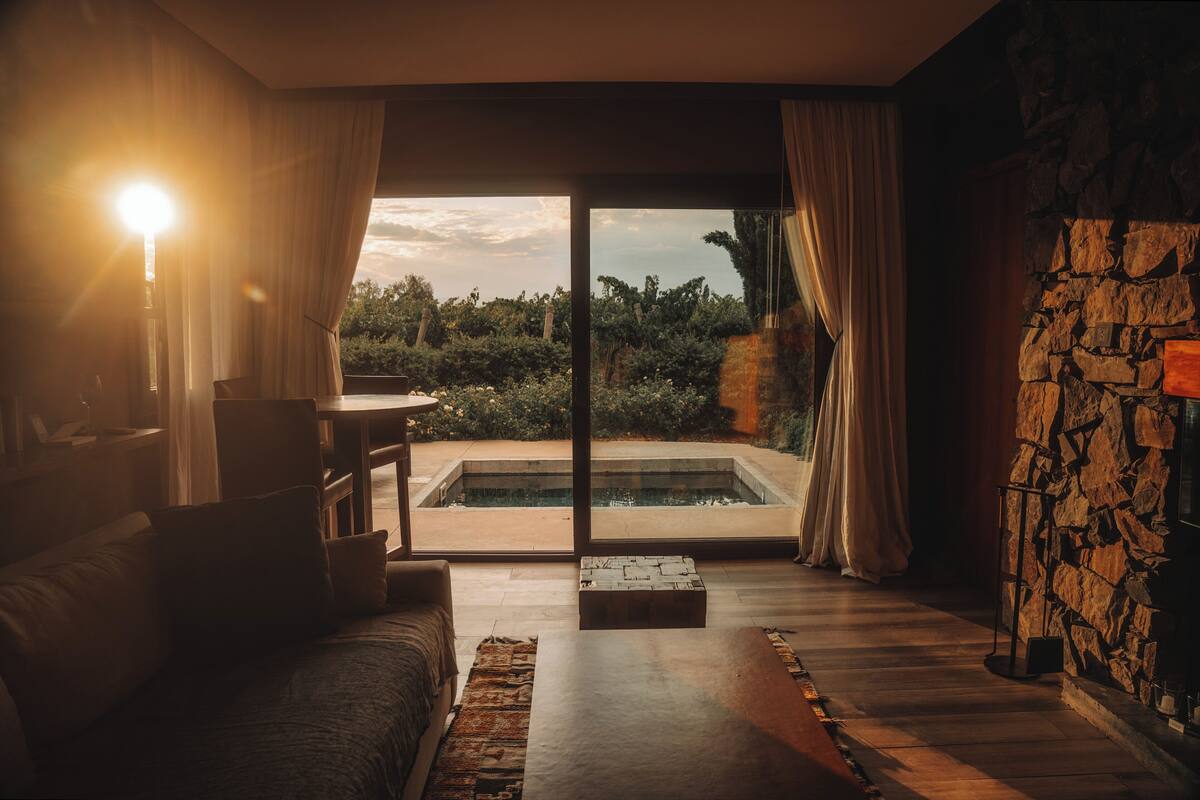 A room with a large sliding glass door leading to a pool, a sofa, and a stone wall.