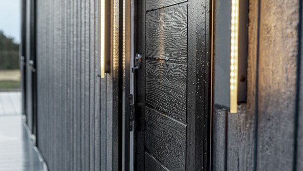 Ein Detailaufnahme einer dunkelbraunen Holztür mit strukturierter Oberfläche und einem Metallgriff.