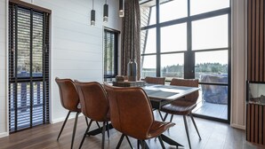 Ein moderner Essbereich mit großem Tisch, Lederstühlen, großen Fenstern mit Jalousien und hängenden Pendelleuchten.