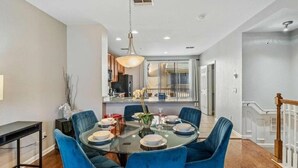 A dining area with a round glass table, blue upholstered chairs, and a hanging light fixture.
