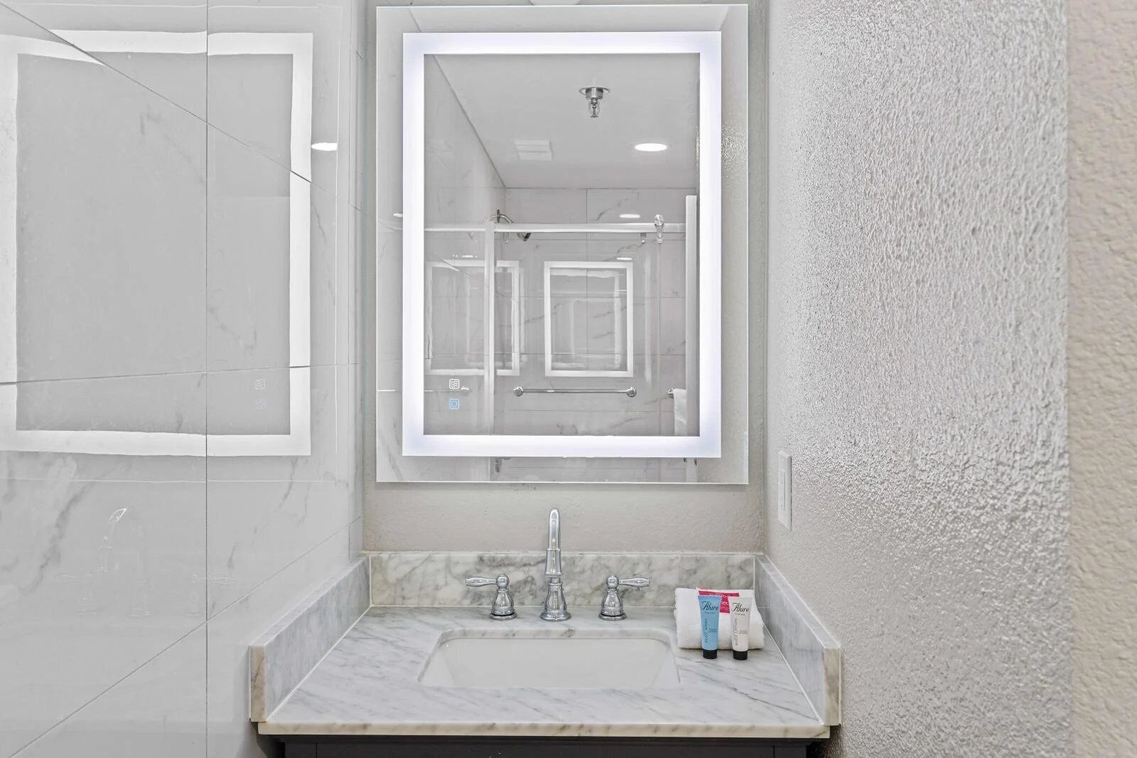 A modern bathroom with a large mirror, a marble sink, and a shower area.