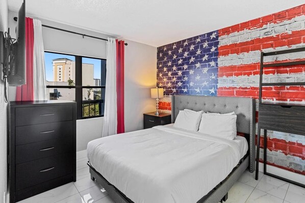 A bedroom with a bed, a dresser, a nightstand, a lamp, and a wall with a brick pattern.
