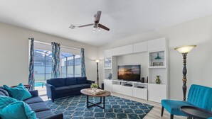 A modern living room with a dark blue sofa, a matching armchair, a coffee table, and a TV on a white entertainment unit.