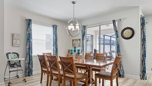 A dining room with a wooden table and chairs, a chandelier, and a view through large windows.