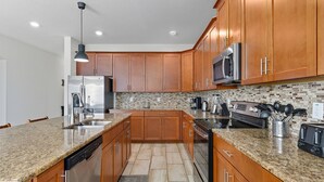 A modern kitchen with granite countertops, wooden cabinets, stainless steel appliances, and a backsplash with mosaic tiles.