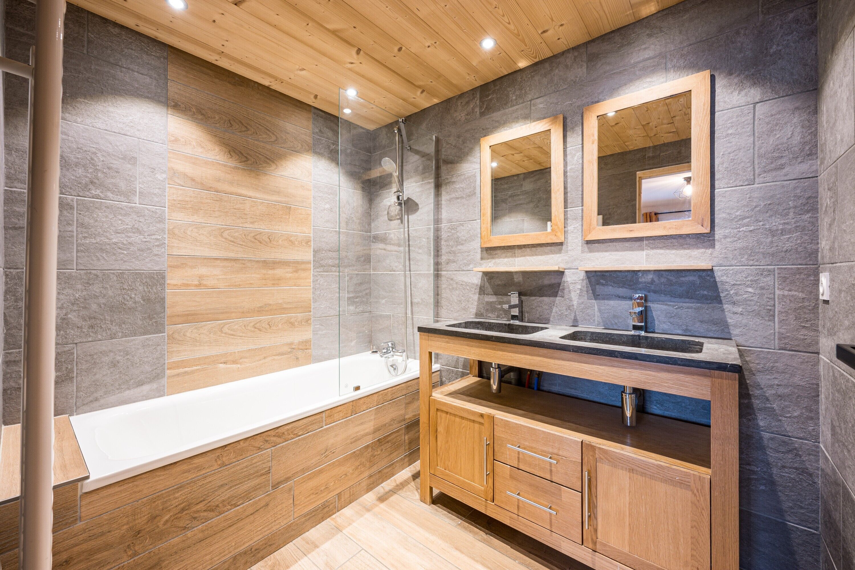 Une salle de bain moderne avec un meuble-lavabo en bois, une baignoire et deux miroirs.