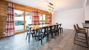A dining area with a long wooden table, black chairs, and a modern light fixture. - Chalet 'Salt Lake' with Mountain View, Private Terrace and Wi-Fi (Fontcouverte-la-Toussuire)