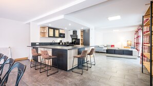 A modern kitchen with a central island, bar stools, and a dining area with a sofa. - Chalet 'Salt Lake' with Mountain View, Private Terrace and Wi-Fi (Fontcouverte-la-Toussuire)
