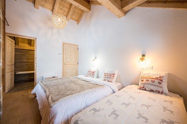 A bedroom with two beds, wooden beams, a wooden wardrobe, and a hanging light fixture.
