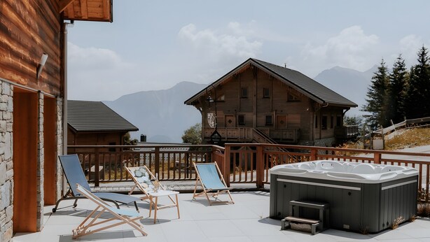 A wooden building with a balcony, lounge chairs, and a hot tub. - Chalet 'Salt Lake' with Mountain View, Private Terrace and Wi-Fi (Fontcouverte-la-Toussuire)