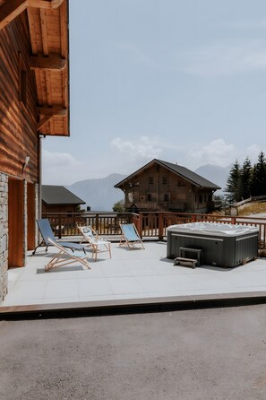 A wooden building with a balcony, lounge chairs, and a hot tub.