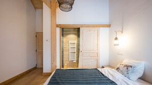 A bedroom with a wooden floor, a bed with a dark blue blanket, a white pillow, a wooden door, and a wall-mounted light fixture. - Chalet 'Salt Lake' with Mountain View, Private Terrace and Wi-Fi (Fontcouverte-la-Toussuire)