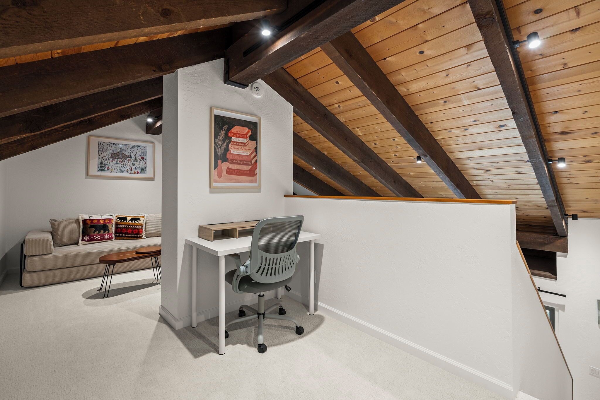 A loft bedroom with a sloped ceiling, a desk, a chair, a sofa, and a framed picture on the wall.