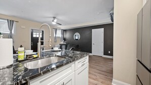 A modern kitchen with a black marble countertop, white cabinets, and a built-in sink. - Cozy King Bed Suite ~ Free Parking & Ground Floor! (Pittsburgh)