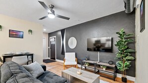 Una sala de estar moderna con un sofá gris, una mesa de centro, un televisor y un ventilador de techo.