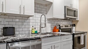 Una cocina moderna con armarios blancos, lavavajillas de acero inoxidable, microondas y horno.