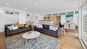 A modern living room with a grey sofa, a coffee table, and a dining area with a table and chairs. - Coastal Style (Lorne)