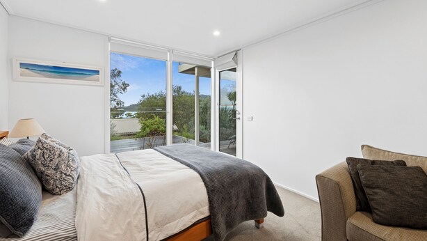 A bedroom with a bed, a chair, a window, and a picture on the wall. - Coastal Style (Lorne)