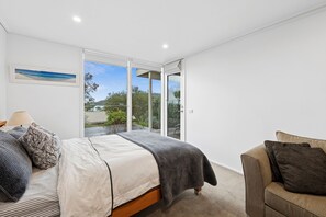 A bedroom with a bed, a chair, a window, and a picture on the wall.