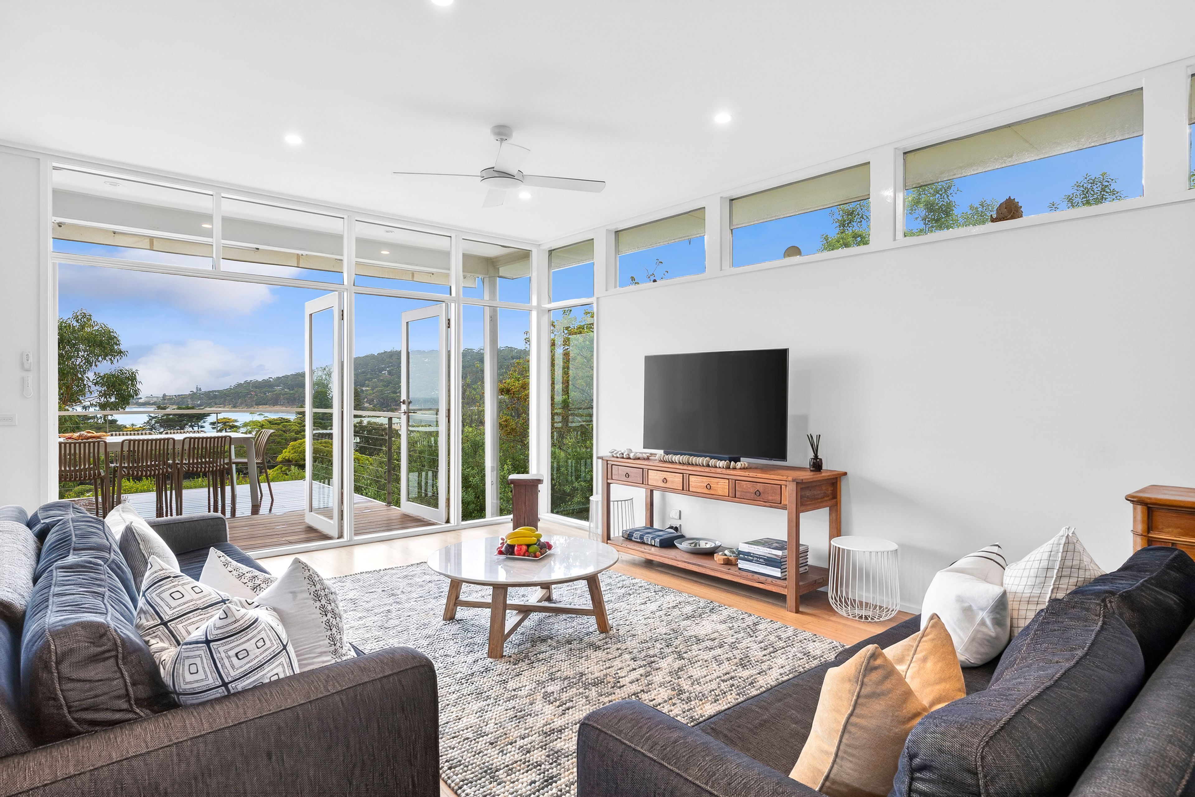 A spacious living room with a large flat-screen TV, comfortable seating, and a balcony with a scenic view.