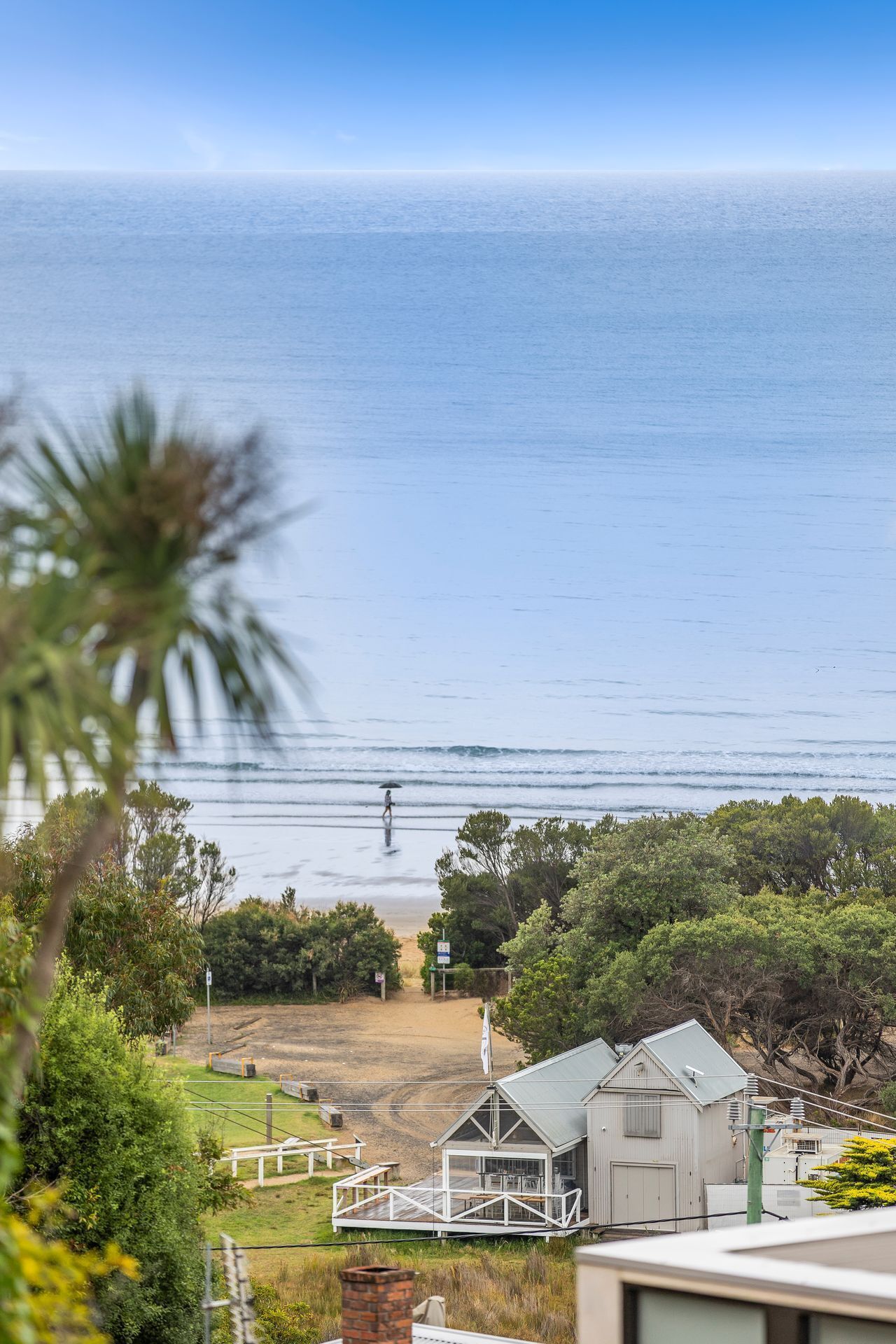 A coastal view with a beach, a person walking with an umbrella, and a building with a deck.