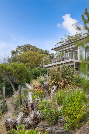 A modern house with a glass balcony overlooking a garden.