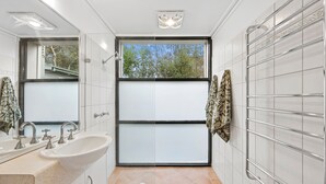Ein modernes Badezimmer mit einem großen Fenster, einem Waschbecken mit zwei Wasserhähnen und einem Spiegel.