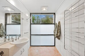 A modern bathroom with a large window, a sink with two faucets, and a mirror.