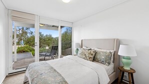 A bedroom with a bed, a nightstand, a lamp, and a view of the outdoors through a sliding glass door. - Coastal Style (Lorne)