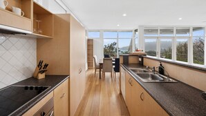 A modern kitchen with wooden cabinets, a black countertop, and a view of the outdoors through large windows. - Coastal Style (Lorne)