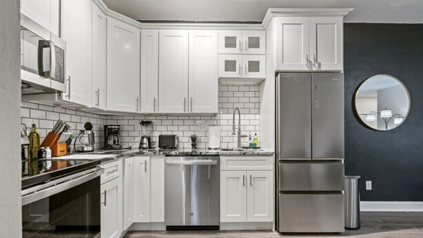 A modern kitchen with white cabinets, stainless steel appliances, and a dark accent wall.