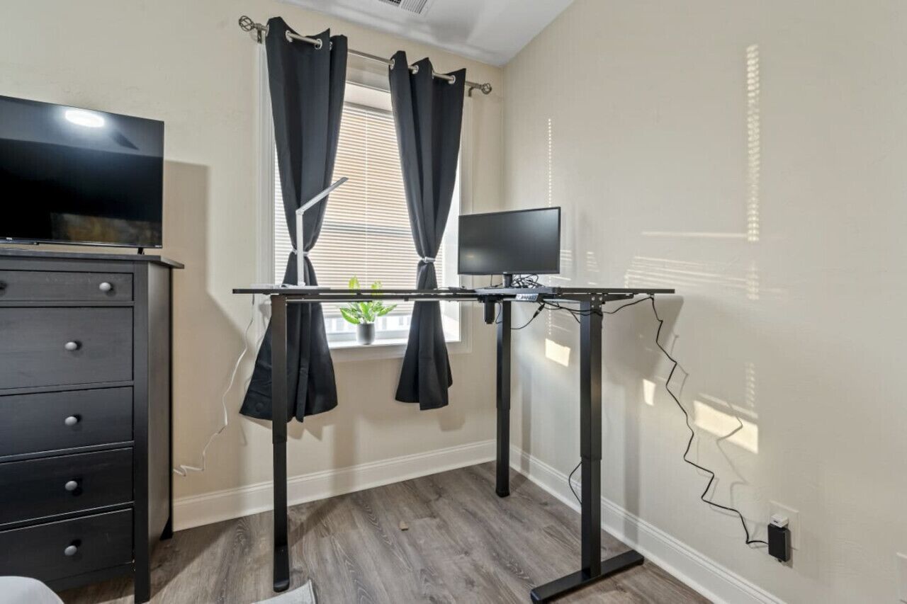 A room with a desk, a television, and a window with curtains.