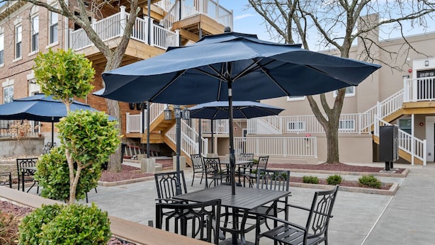 Une terrasse extérieure avec des tables et des chaises, des parasols et un petit arbre.