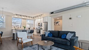 A modern living room with a grey sofa, a round coffee table, and a dining area with a kitchen in the background. - Bright & Upscale|King Bed|Free Parking w/Workspace (Pittsburgh)