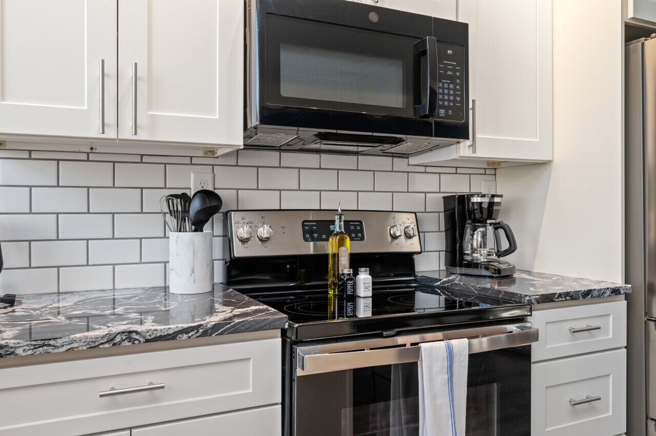 A kitchen with white cabinets, a black microwave, a stove, and a coffee maker.
