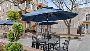 Une terrasse extérieure avec des tables et des chaises, des parasols et un petit arbre.