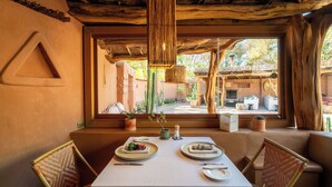 Un coin repas avec une table dressée pour deux personnes, un luminaire suspendu et une vue sur la terrasse extérieure.