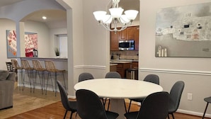 A modern kitchen with stainless steel appliances, a dining area with a round table and chairs, and a chandelier. - Gorgeous house in The Woodlands (Spring)