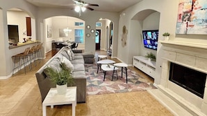 A spacious living room with a sofa, coffee table, and fireplace. There is a television mounted on the wall and a ceiling fan. - Gorgeous house in The Woodlands (Spring)