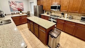 A modern kitchen with granite countertops, wooden cabinets, stainless steel appliances, and a central island. - Gorgeous house in The Woodlands (Spring)