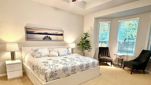 A bedroom with a large bed, two bedside tables, a chair, a small table, and a window with blinds. - Gorgeous house in The Woodlands (Spring)
